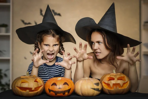 Happy family: mom and daughter celebrate Halloween. Merry people in carnival costumes in the room. Cheerful kids and parents play with pumpkins and black witch hats