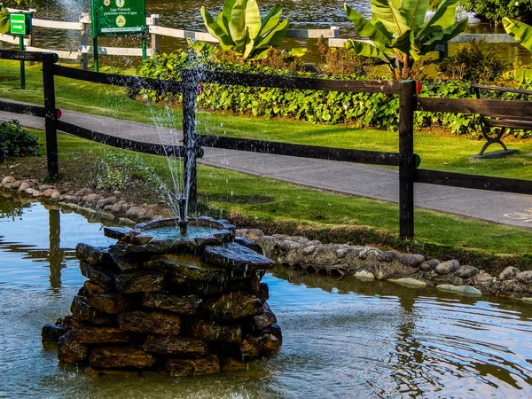 Small fountain in the middle of a pond and a walkway in public park