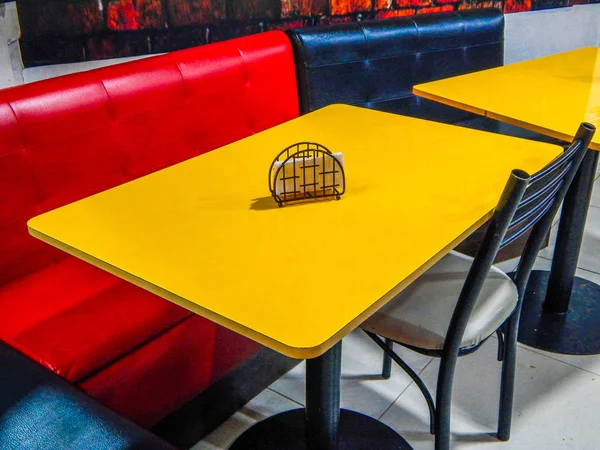 Padded black and red sofas with yellow table and napkin holder over the table