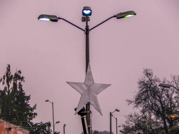 Street pole with three lights and a star in rain with very gray and cloudy sky