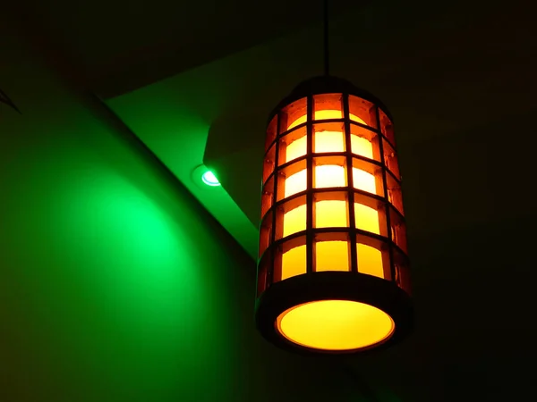 A wooden lamp hanging from plaster ceiling next to a green led light