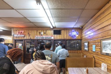 Luling, Teksas, ABD - 15 Mart 2025: Teksas 'ta neon levhaları ve ahşap paneli olan ünlü Luling City Market BBBQ restoranında sırada bekleyen müşteriler