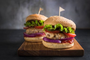 İki ev yapımı hindi burger salata, domates, turşu ve ahşap kesme tahtası üzerinde kırmızı soğan ile