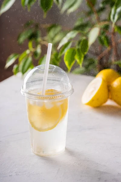 Льодовий лимонад з содовою в пластиковій чашці на столі з лимонами та кубиками льоду. Спортивний напій . Стокове Зображення
