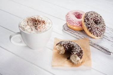 Beyaz ahşap masada krema ile kahve ile pembe ve çikolatalı çörekler.