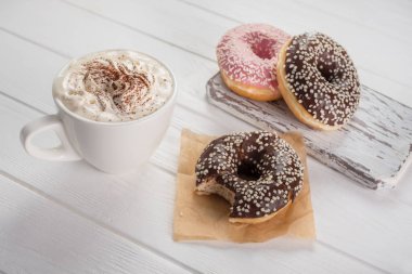 Beyaz ahşap masada krema ile kahve ile pembe ve çikolatalı çörekler.