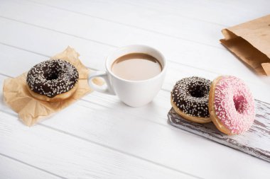 Beyaz ahşap masada krema ile kahve ile pembe ve çikolatalı çörekler.