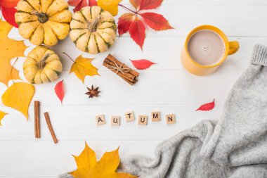 Sonbahar yatağı. Balkabağı, süveter, kakaolu kupa ve beyaz ahşap arka planda sarı yapraklar. Tahta kelime Sonbahar .