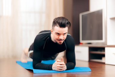 Adam kalas pozisyonunda, evde egzersiz yapıyor. 