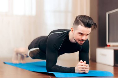 Adam kalas pozisyonunda, evde egzersiz yapıyor. 