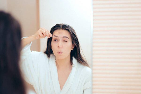 Woman Wearing Bathrobe Plucking her Eyebrows After Shower