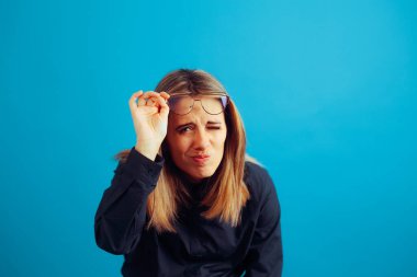 Bir kadın gözlüğünü çıkarıp gözlerini kıstı. 