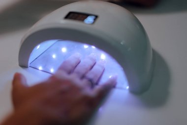 Ultraviyole lambada jel manikürü yaptıran bir kadının eli