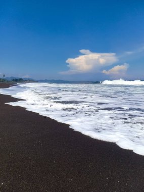 güzel manzara, deniz köpüğü ve beyaz bulutlar mavi gökyüzünde, güneşli gün Amed plaj, Bali Adası üzerinde form dalgalar tarafından yıkanmış siyah volkanik kum Hint Okyanusu kıyısında.