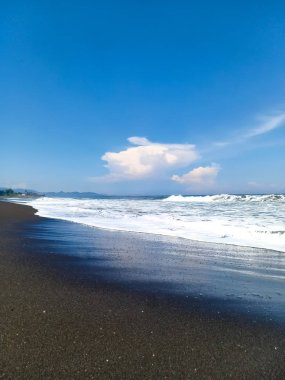 güzel manzara, deniz köpüğü ve beyaz bulutlar mavi gökyüzünde, güneşli gün Amed plaj, Bali Adası üzerinde form dalgalar tarafından yıkanmış siyah volkanik kum Hint Okyanusu kıyısında.