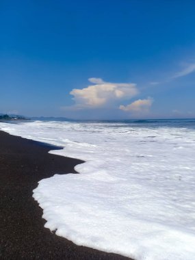güzel manzara, deniz köpüğü ve beyaz bulutlar mavi gökyüzünde, güneşli gün Amed plaj, Bali Adası üzerinde form dalgalar tarafından yıkanmış siyah volkanik kum Hint Okyanusu kıyısında.