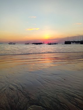 Islak kum Hint Okyanusu kıyısında çok güzel bir gün batımı yansıyan iskele ve Balık tutma gemi görülebilir. 26 Şubat, Bali, Endonezya.