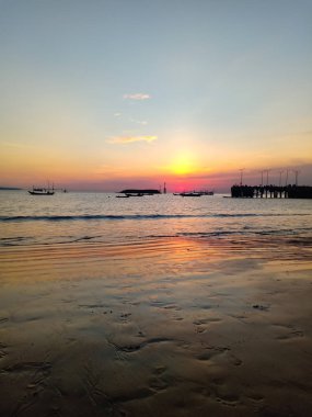 Islak kum Hint Okyanusu kıyısında çok güzel bir gün batımı yansıyan iskele ve Balık tutma gemi görülebilir. 26 Şubat, Bali, Endonezya.