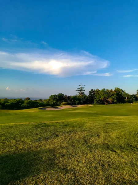 Beautiful green golf course in exotic island Bali at sunset. Green field, blue sky and white clouds. Indonesia 03/05/2019