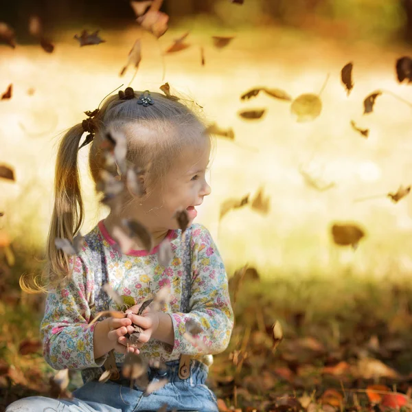 秋の公園で遊ぶ白ダウン症候群の女の子の葉します — ストック写真