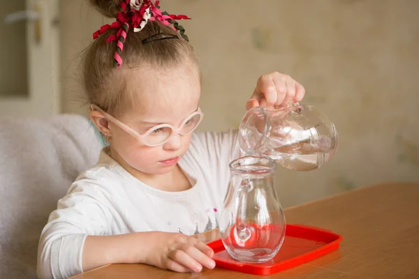 ダウン症候群の女の子は優しく水差しに水差しから水を注ぐ — ストック写真