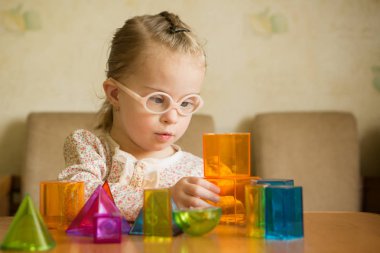 Girl with Down syndrome playing with geometrical shapes clipart