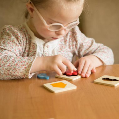 smart girl with Down syndrome collects puzzles clipart