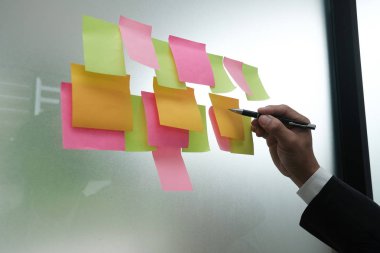 İşadamı işyerinde cam duvar üzerine yapışkan notlar yazmak. Yapışkan Not kağıt hatırlatma programı yaratıcı fikir ve iş beyin fırtınası tartışmak için