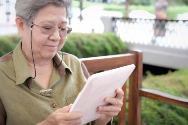 Yaşlı kadın holding tablet. Yaşlı üst düzey kadın manifatura mesaj, touchpad açık havada ile App kullanarak