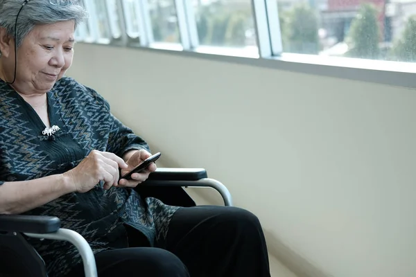 elder woman in wheelchair holding mobile phone. elderly senior female texting message, using app with smartphone at home