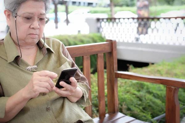 elder woman holding mobile phone. elderly senior female texting message, using app with smartphone outdoors