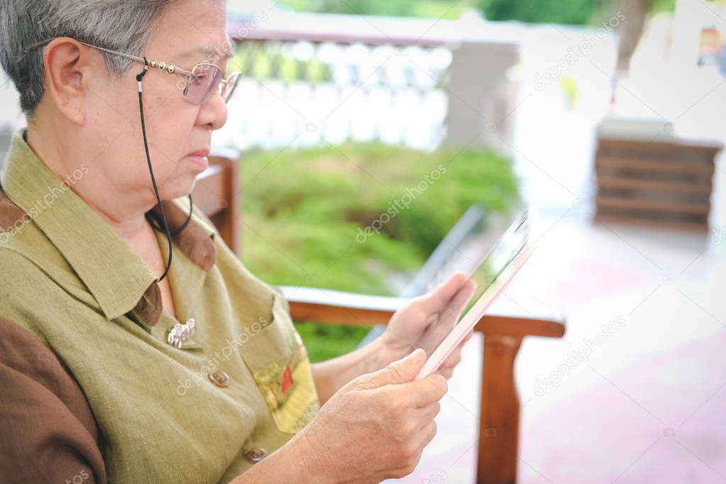 elder woman holding tablet. elderly senior female texting message, using app with touchpad outdoors