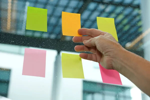 hand hold adhesive notes on glass wall at workplace. Sticky note paper reminder schedule for creative idea & business brainstorming