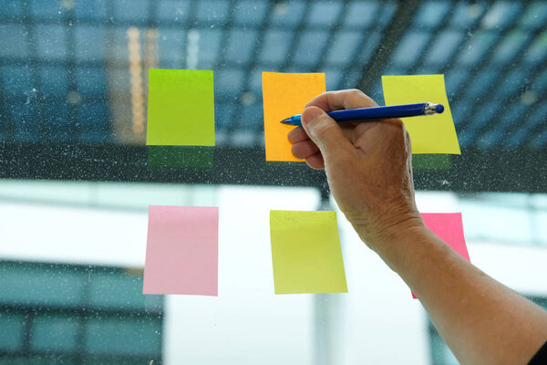 Businessman write on adhesive notes on glass wall at workplace. Sticky note paper reminder schedule for discussing creative idea & business brainstorming