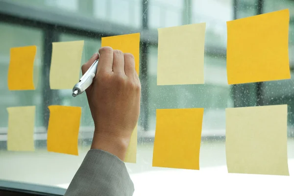 Businessman write on adhesive notes on glass wall at workplace. Sticky note paper reminder schedule for discussing creative idea & business brainstorming