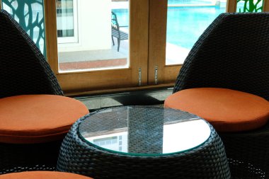 yüzme havuzu yanında modern evde oturma odasında turuncu yastık ile rahat rattan koltuk