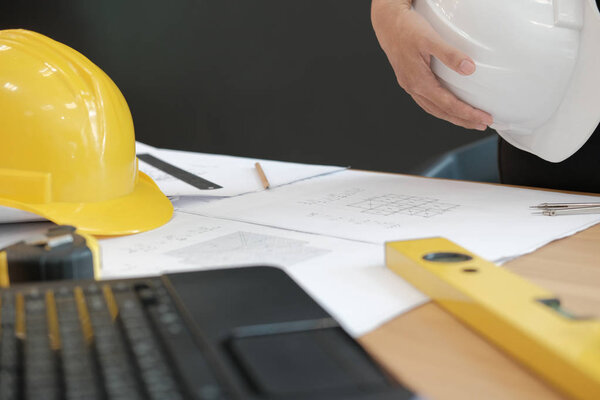 engineer architect worker holding safety helmet hardhat wtih construction blueprint on desk at workplace