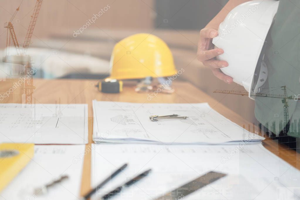 engineer architect worker holding safety helmet hardhat wtih construction blueprint on desk at workplace
