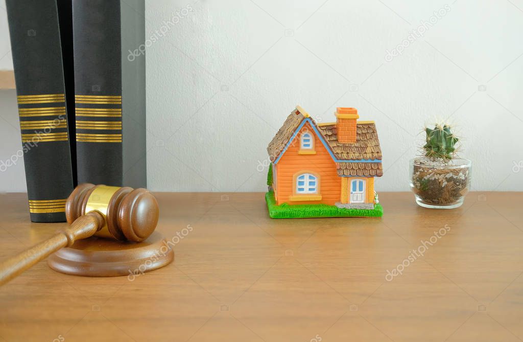 judge gavel law book & home house model on wooden desk near white brick wall. real estate dispute & property auction concept