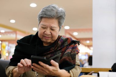 restoranda cep telefonu tutan Asya yaşlı kadın. Yaşlı kıdemli kafede Smartphone kullanarak. Yaşlı kadın manifatura mesaj ile cep telefonu