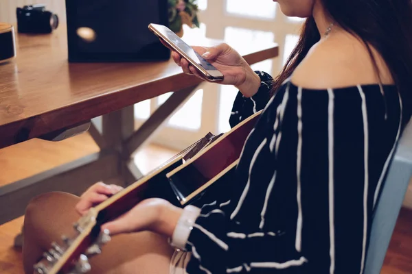 Женщина играет на гитаре с помощью мобильного смартфона — стоковое фото
