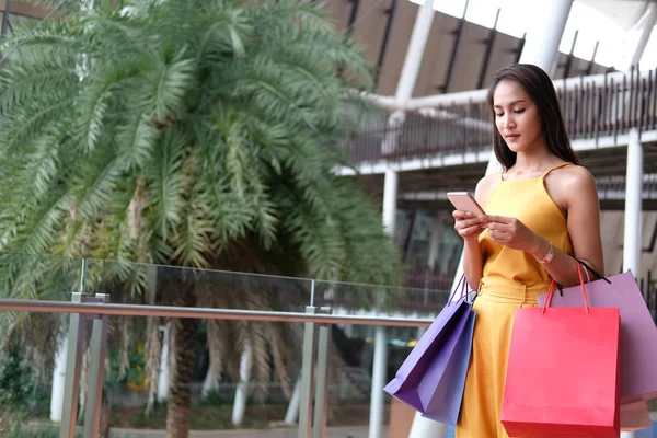 Mujer usando smartphone sosteniendo bolsas de compras. consumismo estilo de vida — Foto de Stock