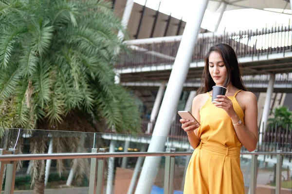 Vrouw met koffiekopje en smartphone buiten — Stockfoto