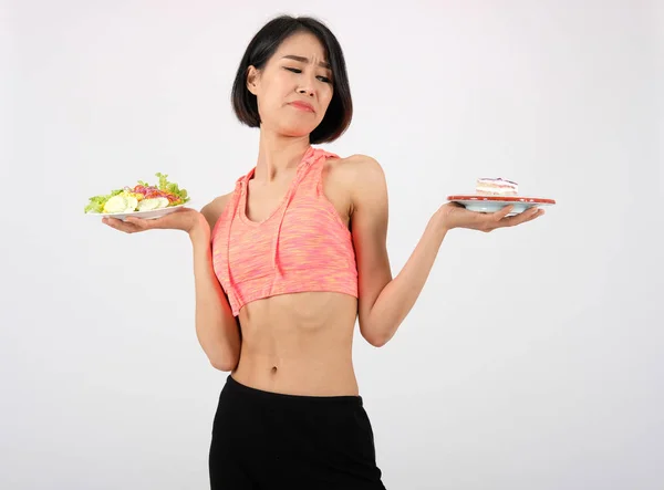 Femme de fitness sportive en vêtements de sport avec salade de légumes et gâteau o — Photo