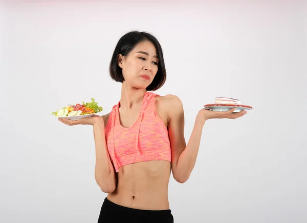 Femme de fitness sportive en vêtements de sport avec salade de légumes et gâteau o — Photo