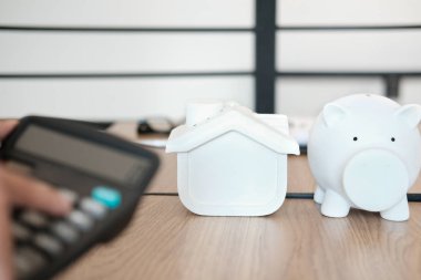 Hesap makinesiyle el hesaplaması. Ev modeli domuz kumbarası masanın üstünde.