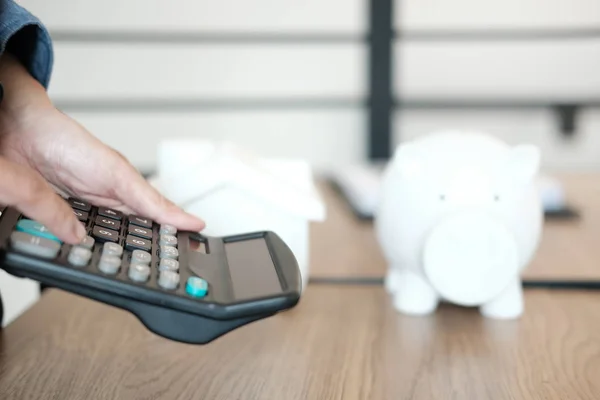 hand calculating with calculator. house model piggy bank on desk