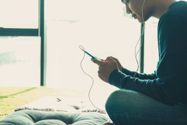 Asyalı genç adam akıllı cep telefonundan müzik dinliyor.