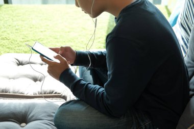 Asyalı genç adam akıllı cep telefonundan müzik dinliyor.