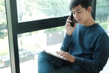 Ofiste cep telefonuyla konuşan serbest çalışan bir erkek. Asyalı f